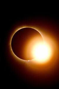 A dramatic photograph capturing the moment of a solar eclipse, where the moon partially covers the sun, creating a bright corona effect around the dark silhouette of the moon.